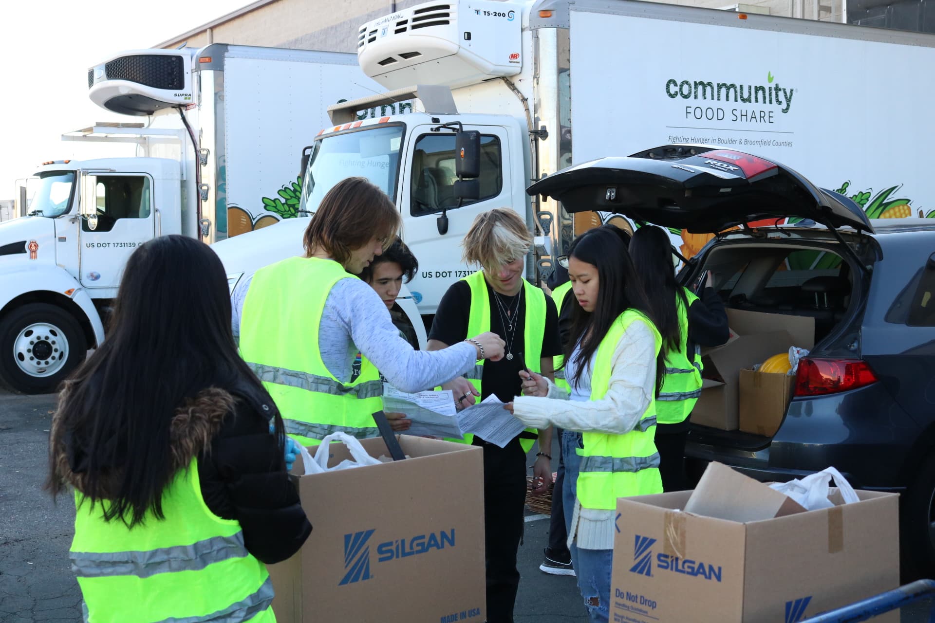 Young volunteers in safety vests checking a list beside a Community Food Share truck
